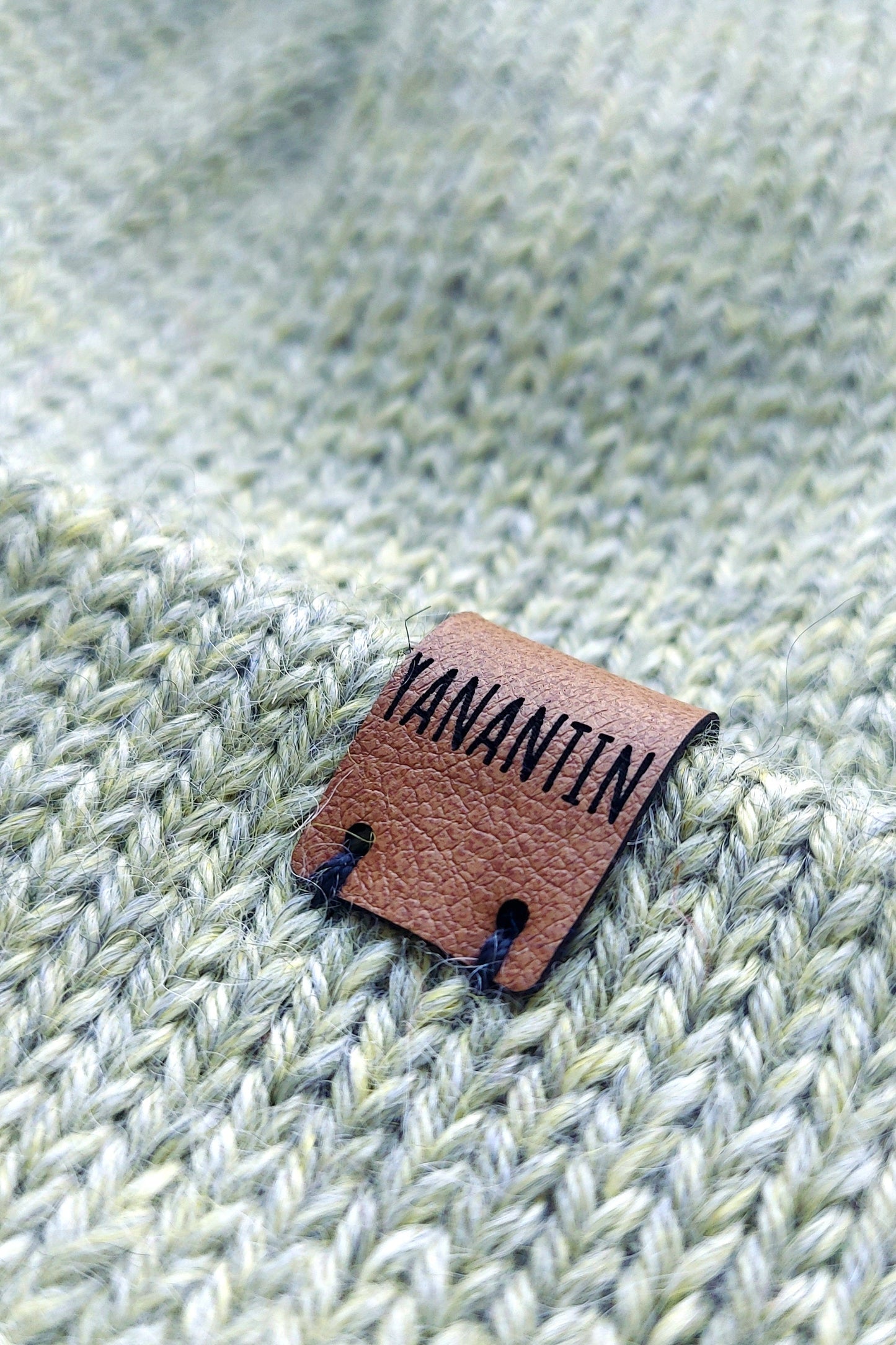 Close-up of the brown vegan leather label on the handmade light green baby hat, highlighting its quality and style.