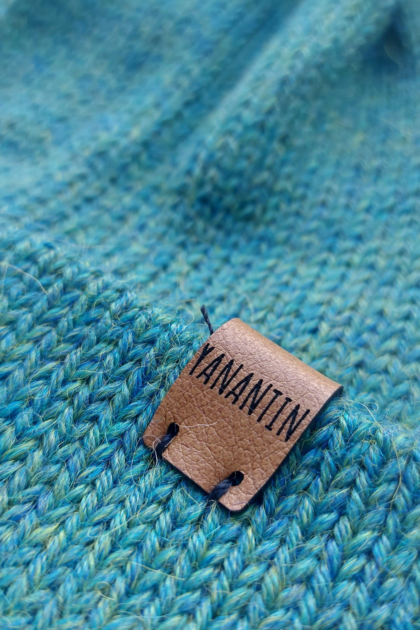 Close-up of the brown vegan leather label on the handmade peacock blue baby hat.