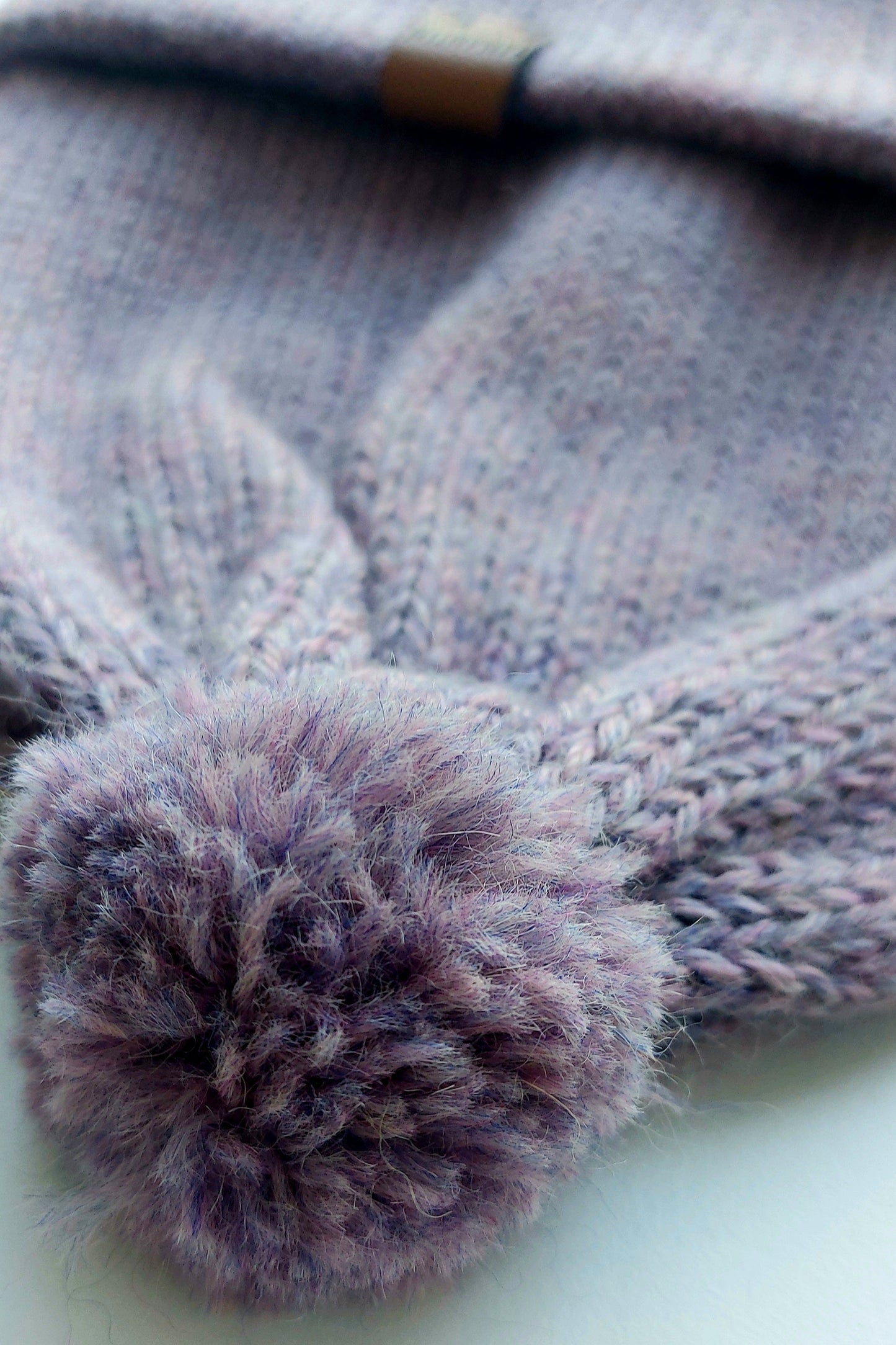 Close-up of the pompom on the handmade lila baby hat, made from soft 100% baby alpaca wool with a foldable edge and brown vegan leather label.