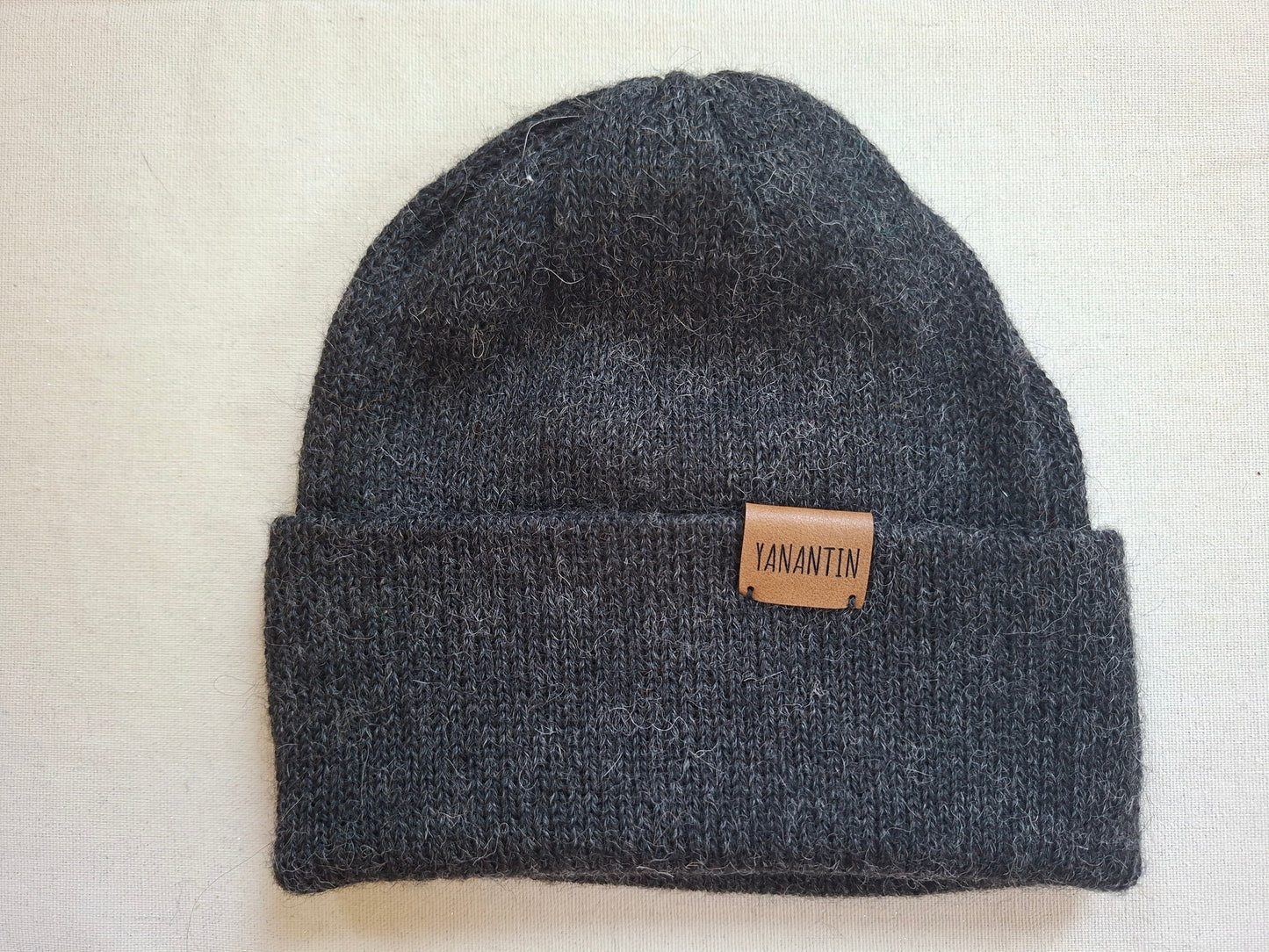 Gray knit beanie with a brown leather patch on a light beige background