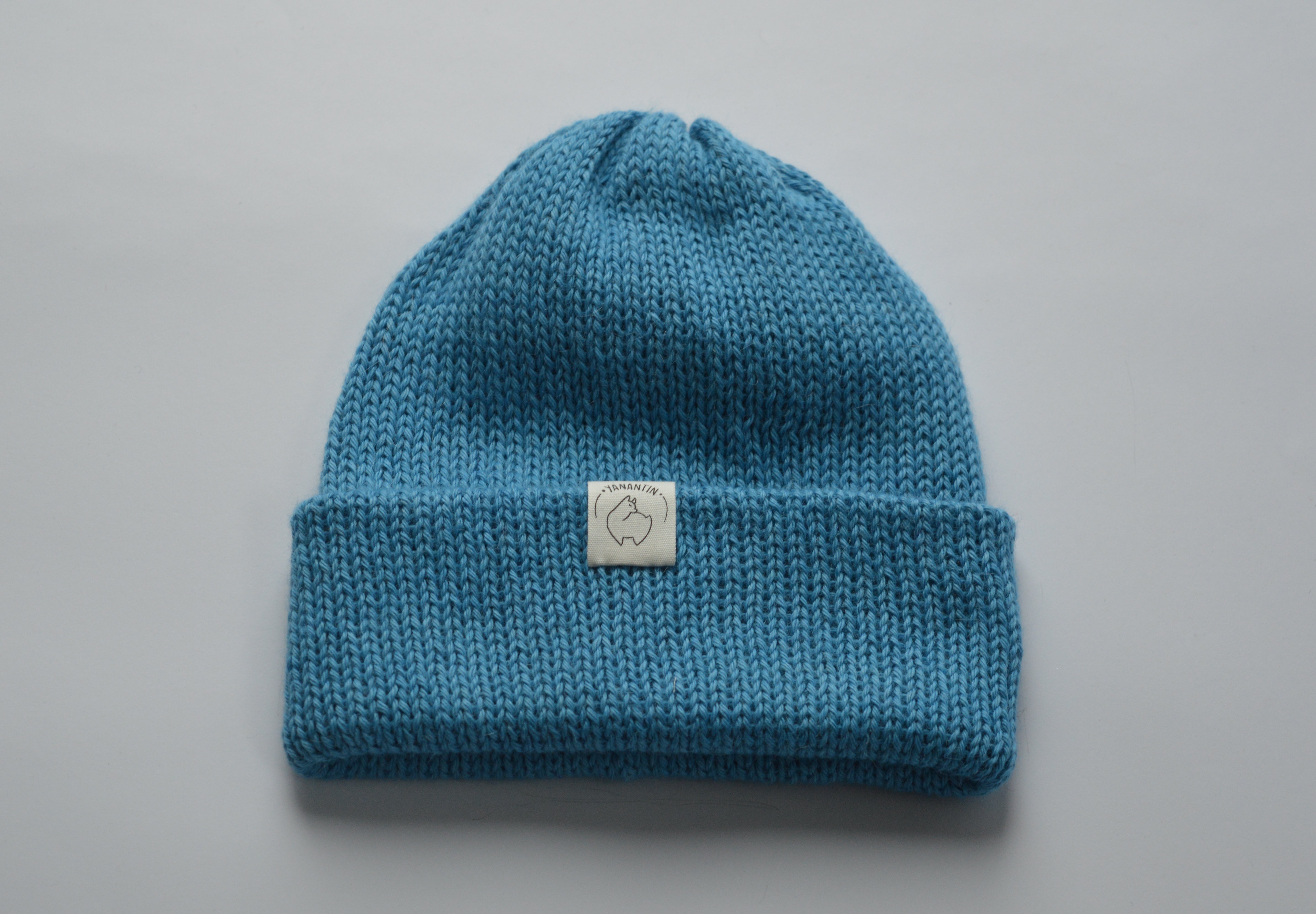 Blue knitted baby alpaca hat with a white organic cotton label and folded brim