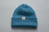 Blue knitted baby alpaca hat with a white organic cotton label and folded brim