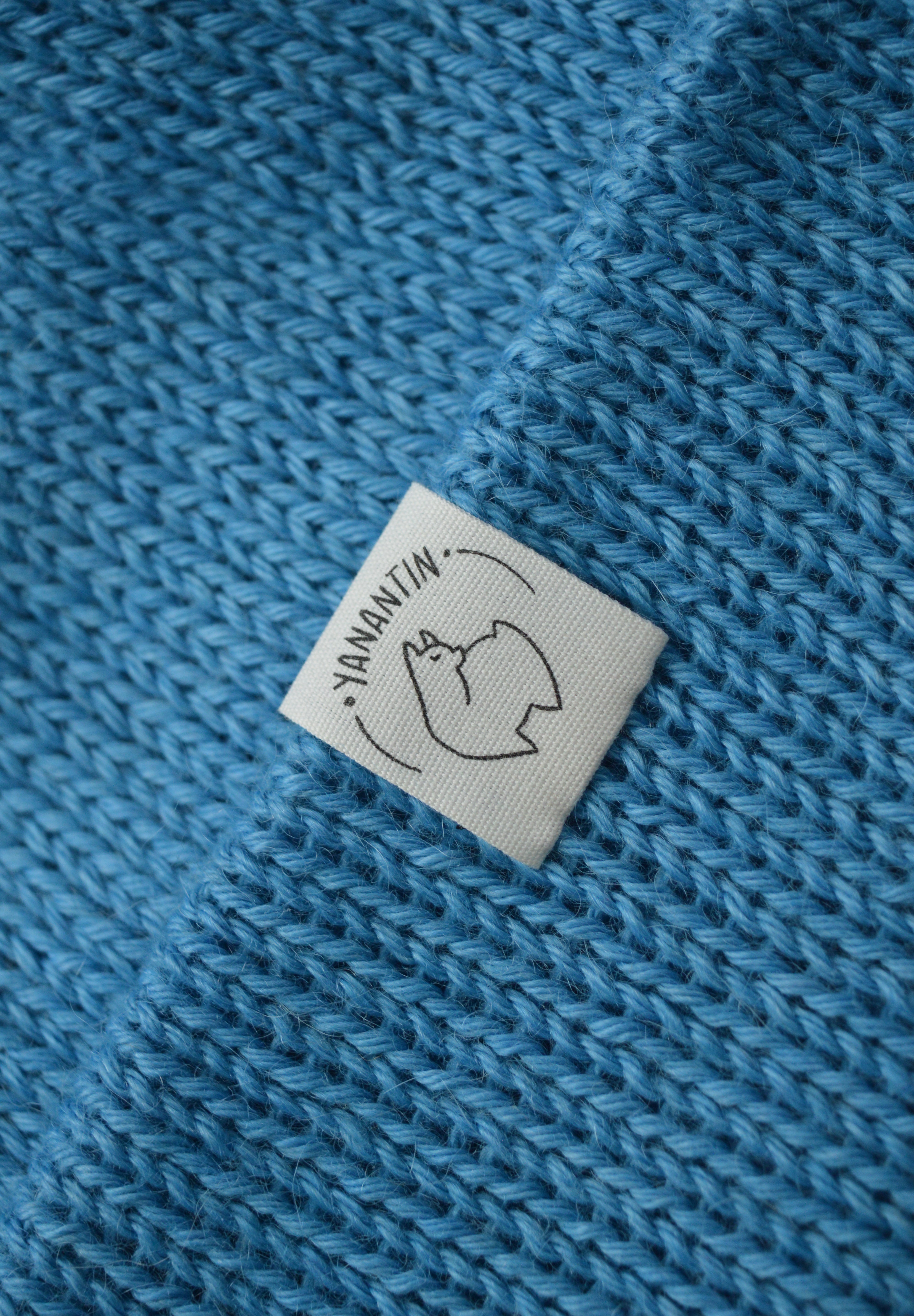 White organic cotton logo of a cute alpaca featuring the brand 'YANANTIN' on a blue woolen hat