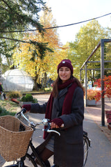 Young woman on a bike wearing a burgondy red alpaca knitwear set: hat, scarf, and mittens.