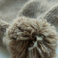 Close-up of the fluffy pompom on a light brown knitted baby hat, made from 100% baby alpaca wool.