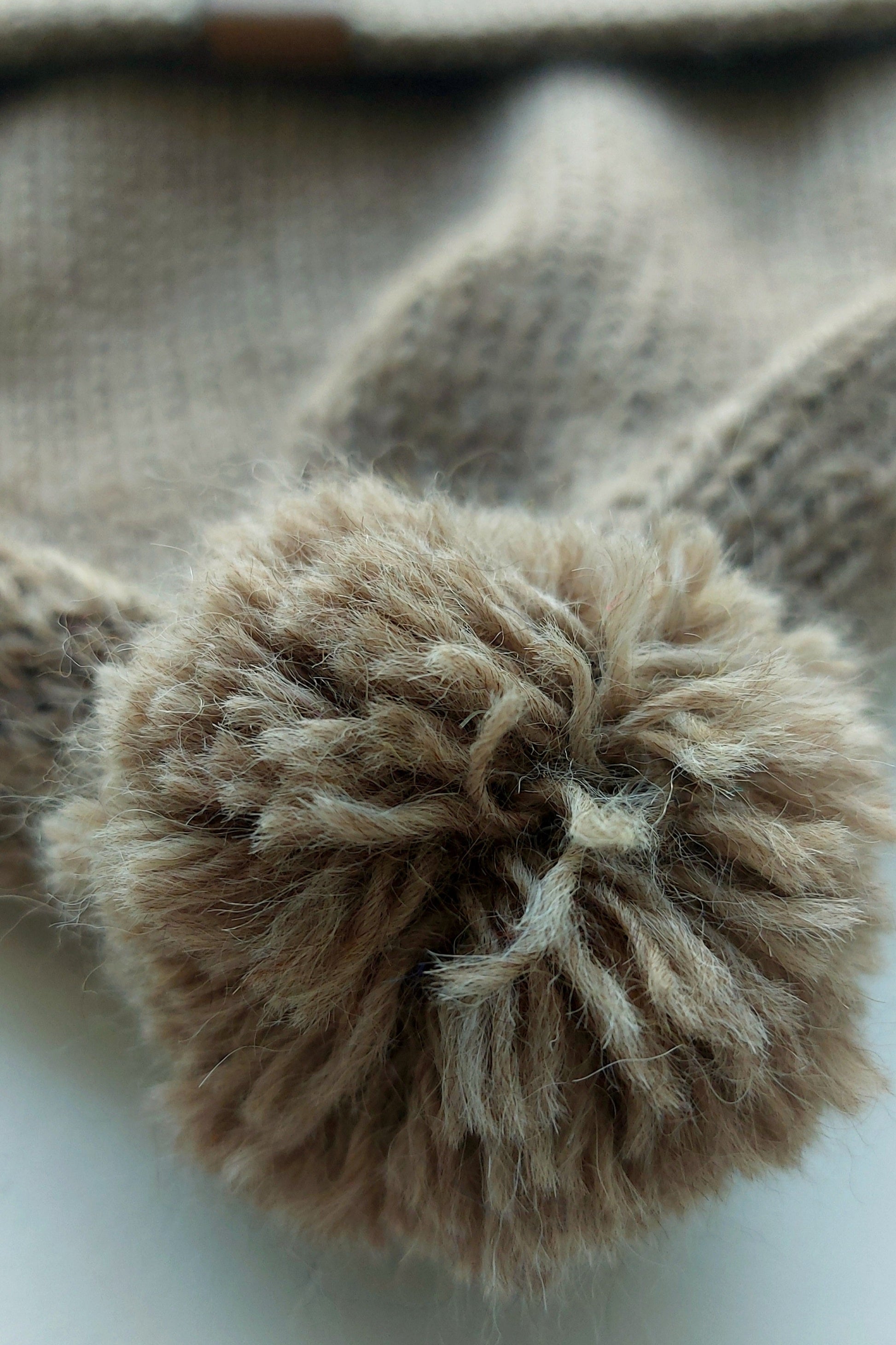 Close-up of the fluffy pompom on a light brown knitted baby hat, made from 100% baby alpaca wool.