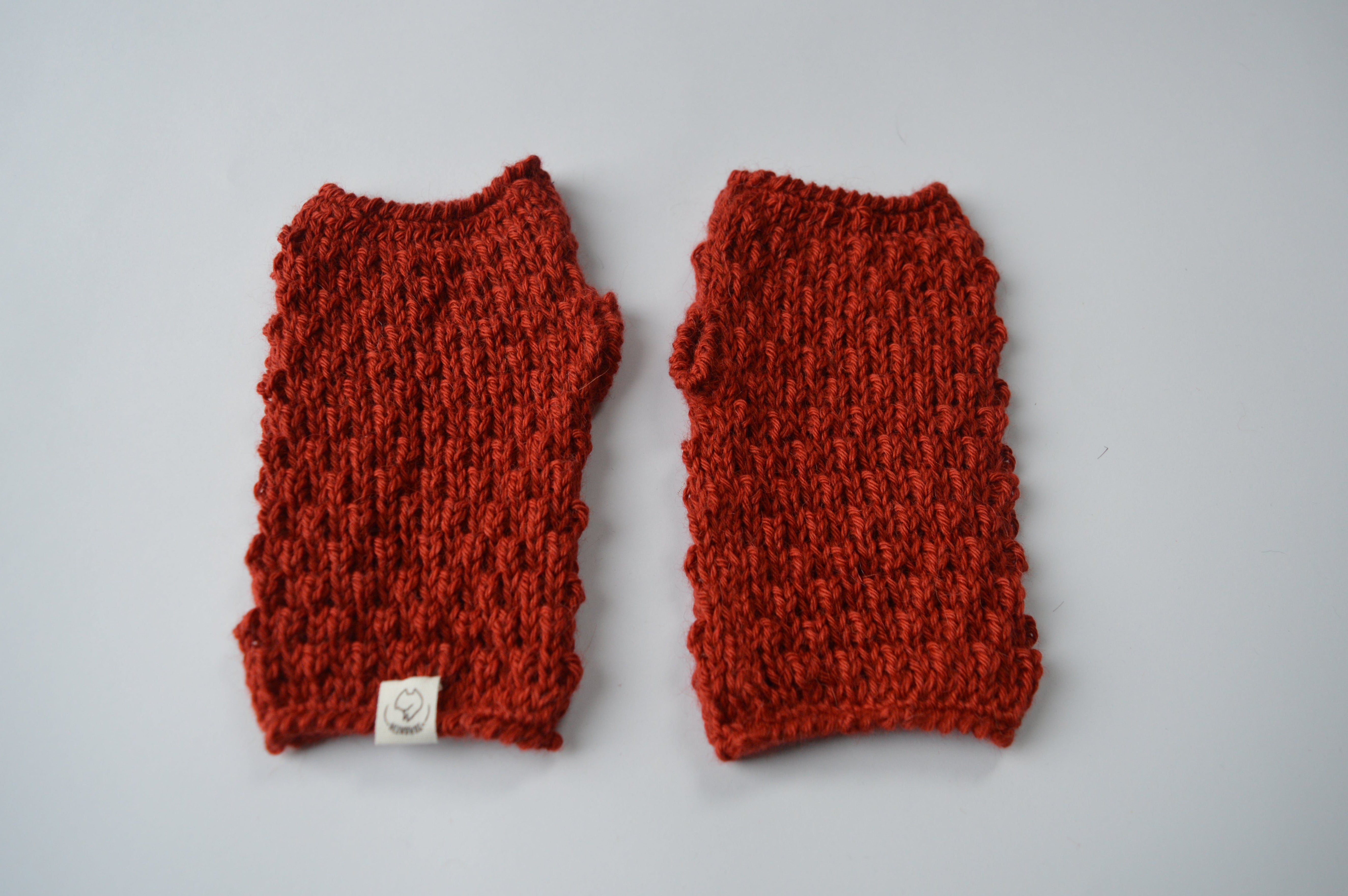 Pair of red knitted fingerless gloves  with crochet borders and an organic cotton label on a light background