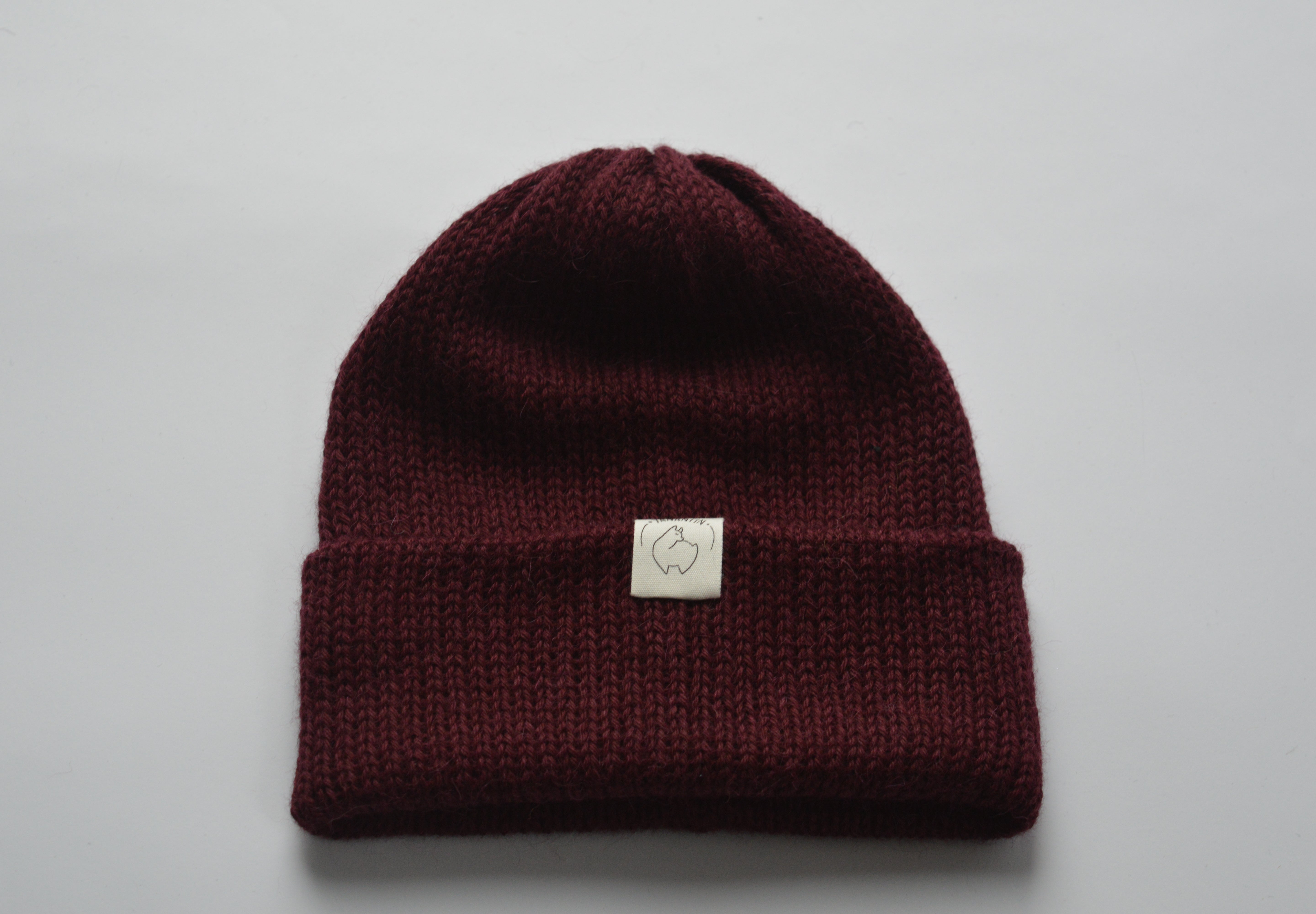 Burgundy red knitted baby alpaca hat with a white organic cotton label and folded brim