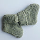 Handmade knitted baby socks in light green with folded ankle cuffs, made from 100% baby alpaca wool—soft, stretchy, and perfect for little feet.
