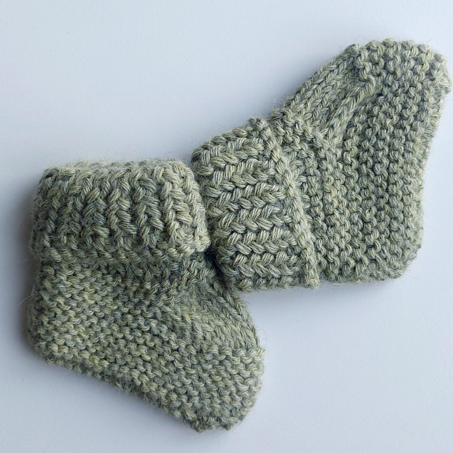 Handmade knitted baby socks in light green with folded ankle cuffs, made from 100% baby alpaca wool—soft, stretchy, and perfect for little feet.
