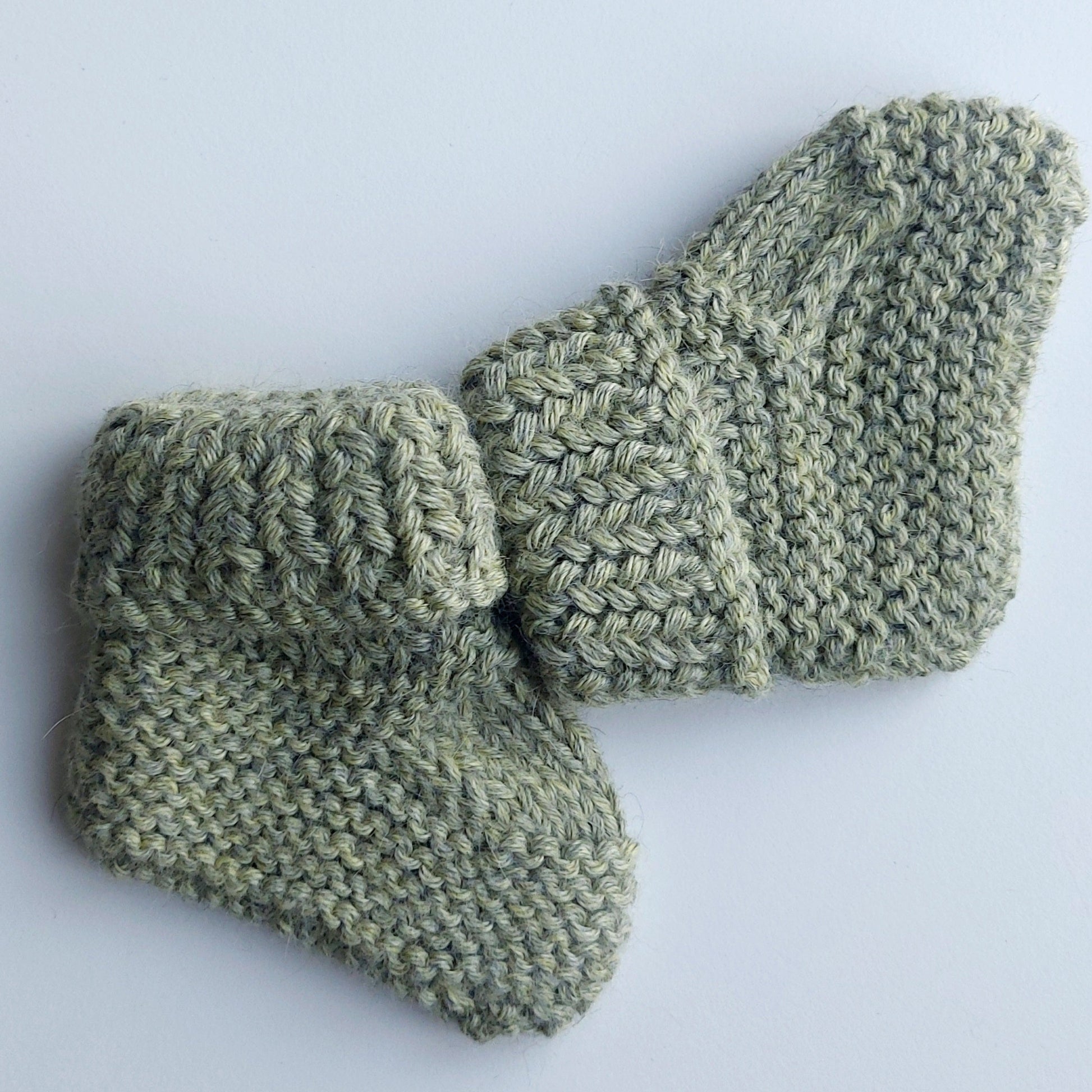 Handmade knitted baby socks in light green with folded ankle cuffs, made from 100% baby alpaca wool—soft, stretchy, and perfect for little feet.
