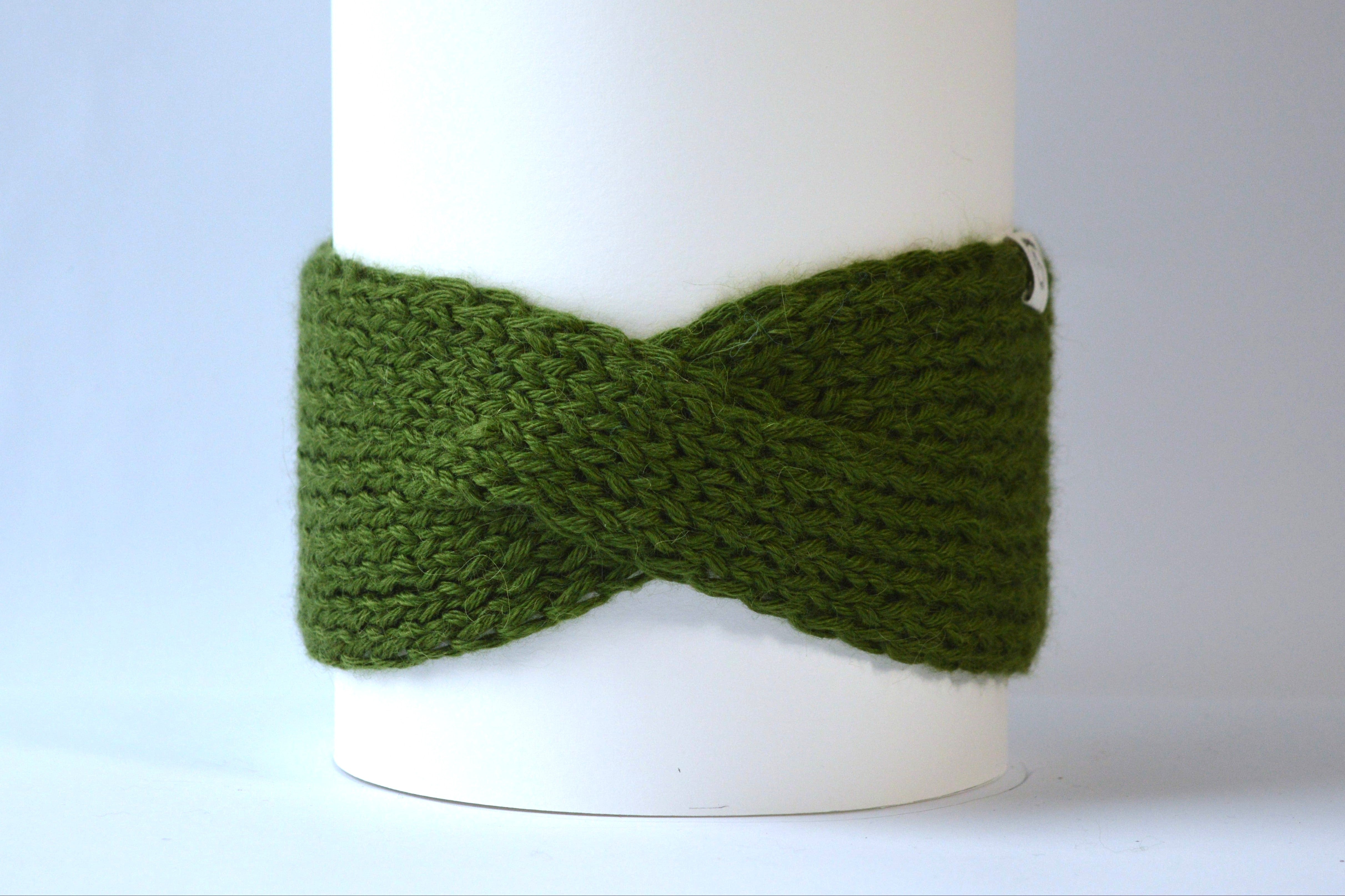 Chunky green knitted headband with a front twist against a gray background