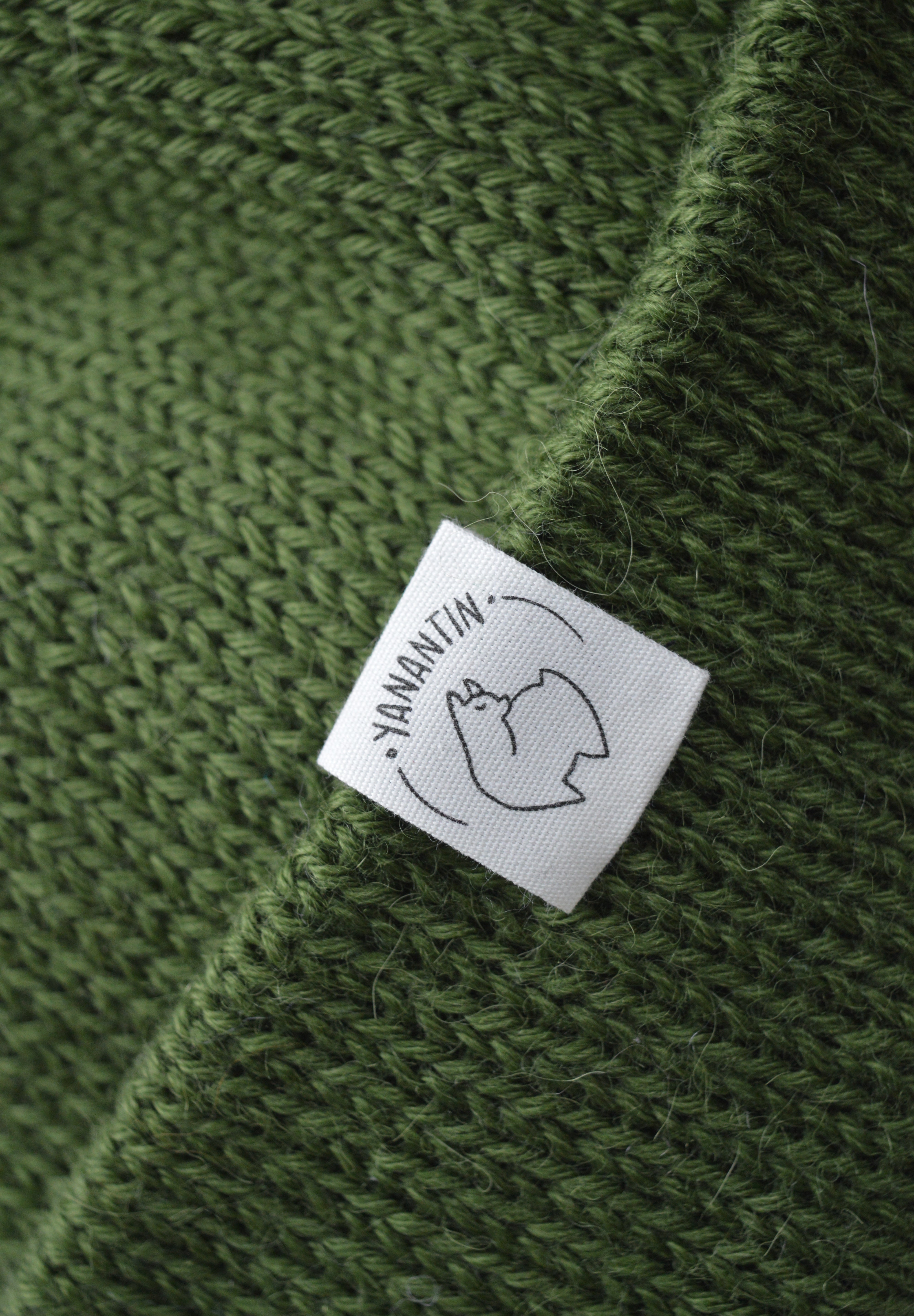 White organic cotton logo of a cute alpaca featuring the brand 'YANANTIN' on a green woolen hat