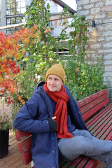 Young male wearing an yellow knitted hat and a yellow scarf sitting on a bench.
