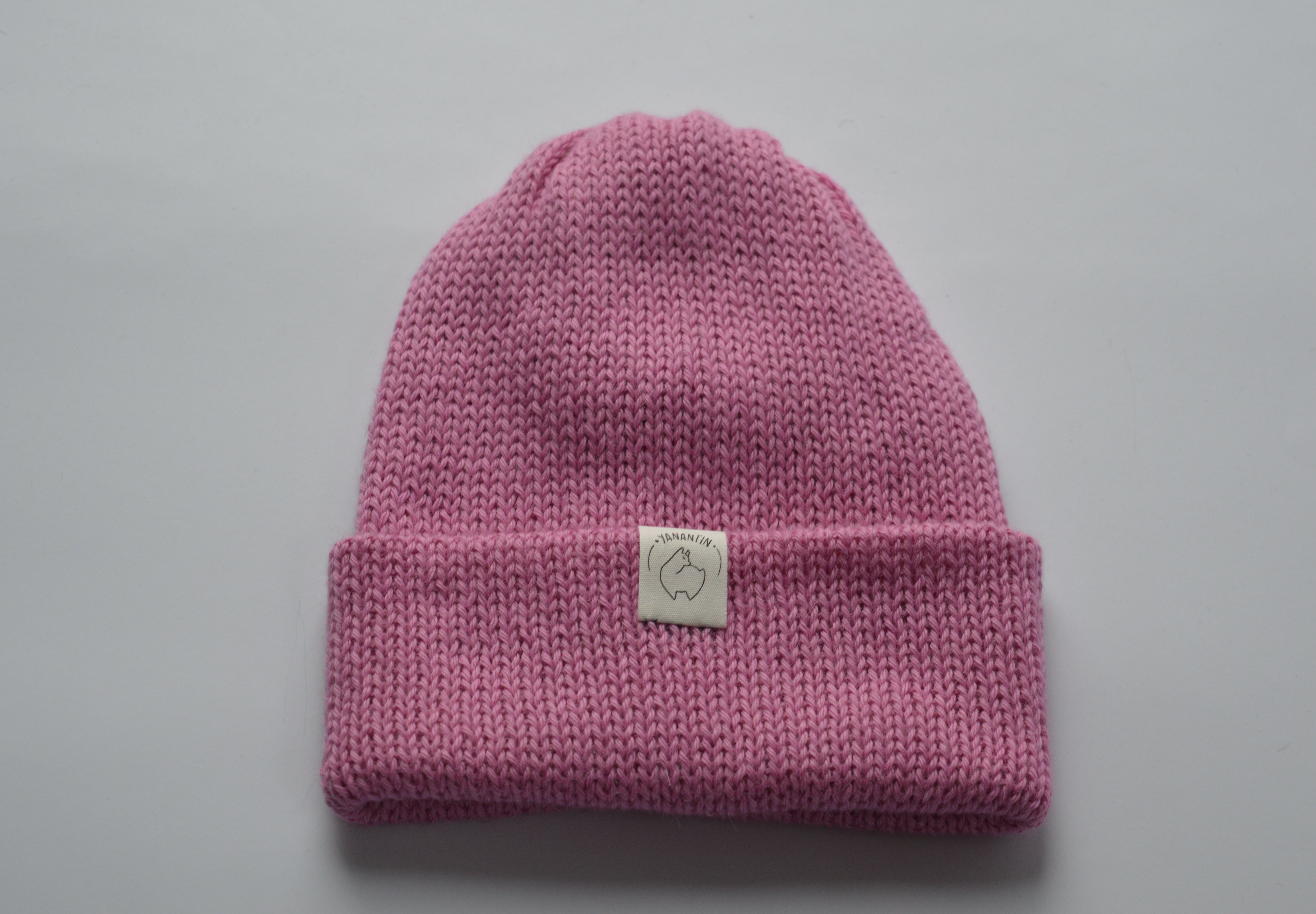 Pink knitted baby alpaca hat with a white organic cotton label and folded brim