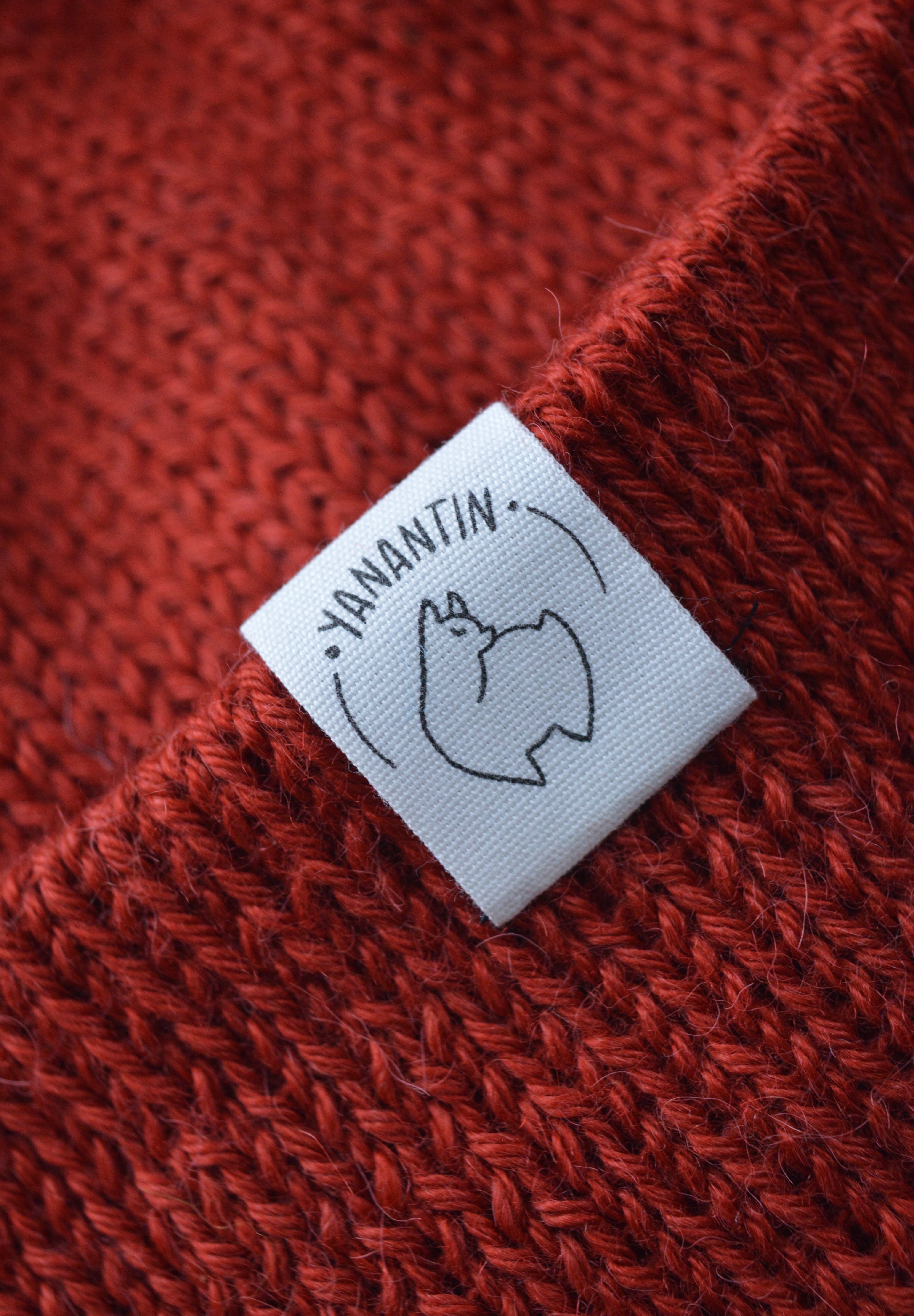 White organic cotton logo of a cute alpaca featuring the brand 'YANANTIN' on a red/orange woolen hat