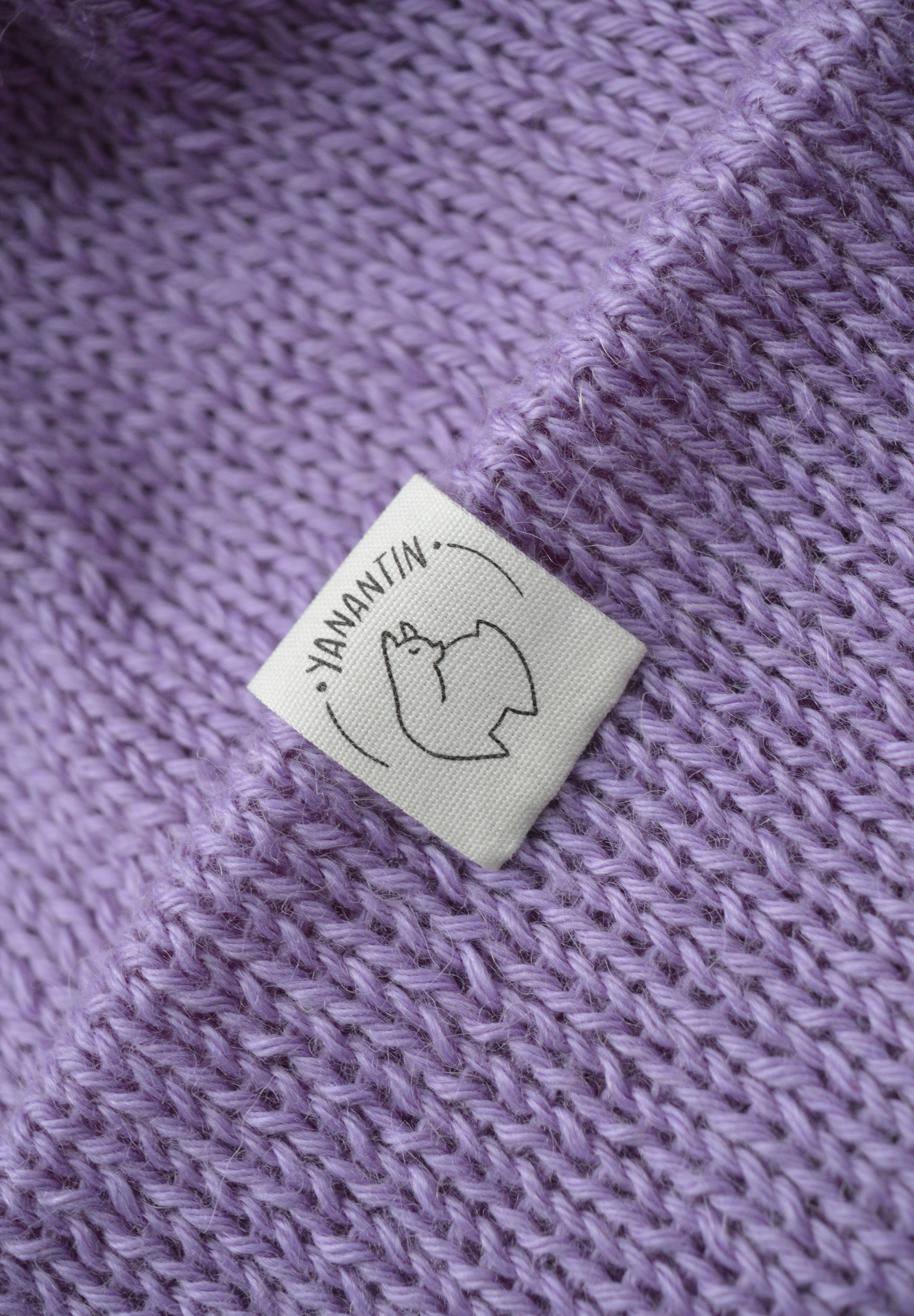 White organic cotton logo of a cute alpaca featuring the brand 'YANANTIN' on a purple woolen hat