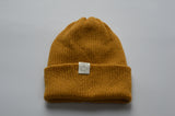 Yellow knitted baby alpaca hat with a white organic cotton label and folded brim