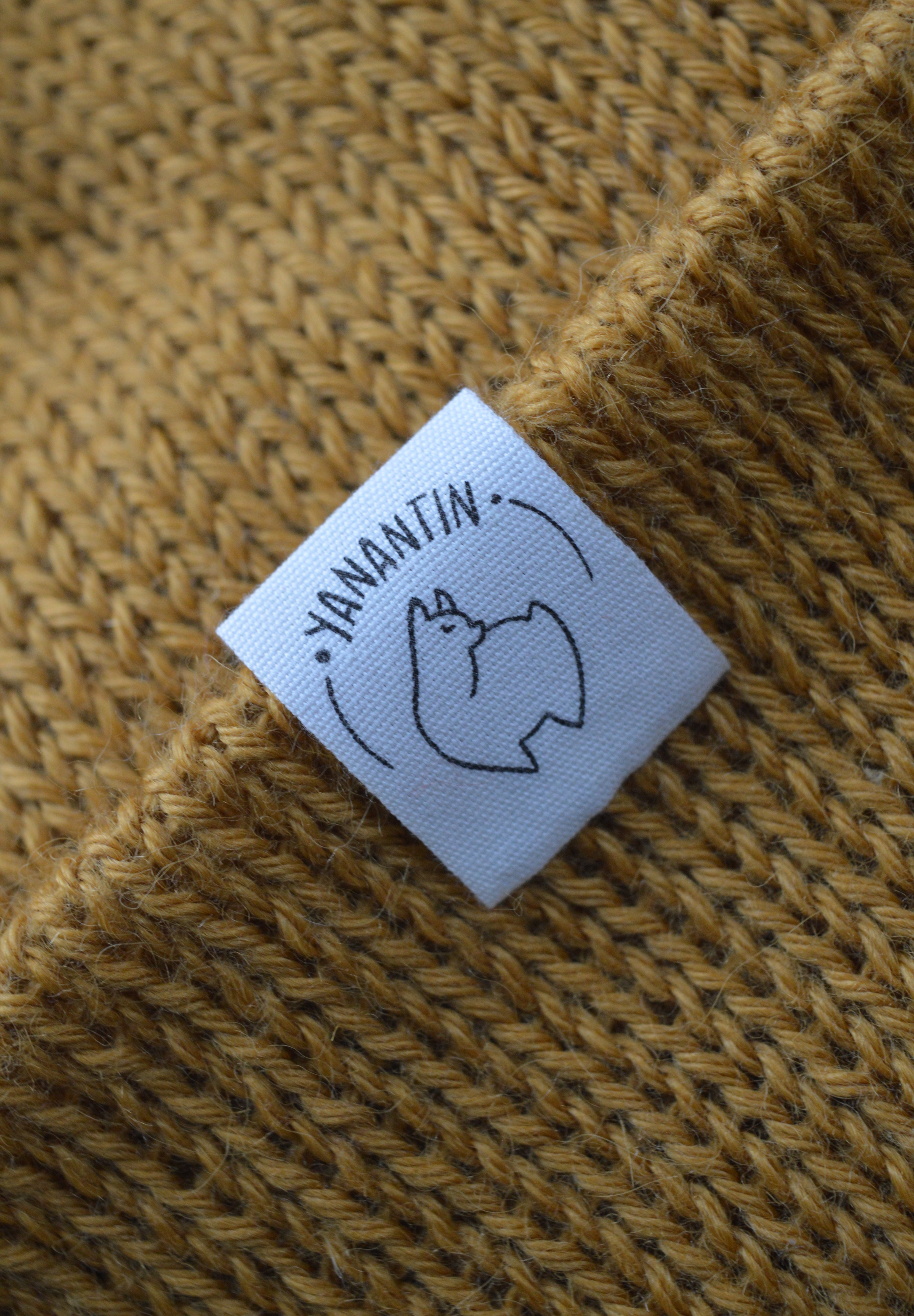 Close-up of a label on a textured mustard yellow knitted hat  of the brand 'YANANTIN'