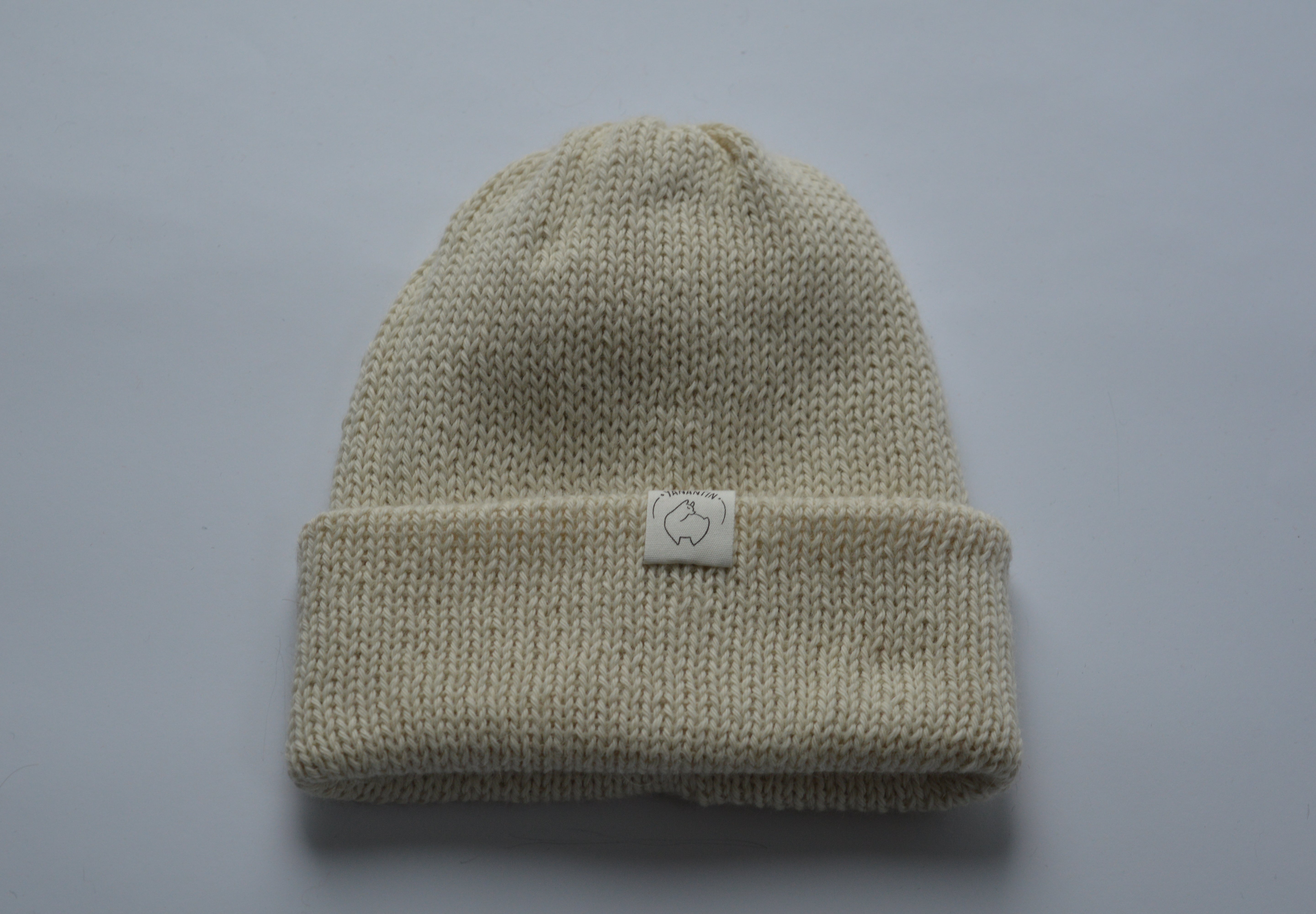 Beige white knitted baby alpaca hat with a white organic cotton label and folded brim