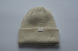 Beige white knitted baby alpaca hat with a white organic cotton label and folded brim