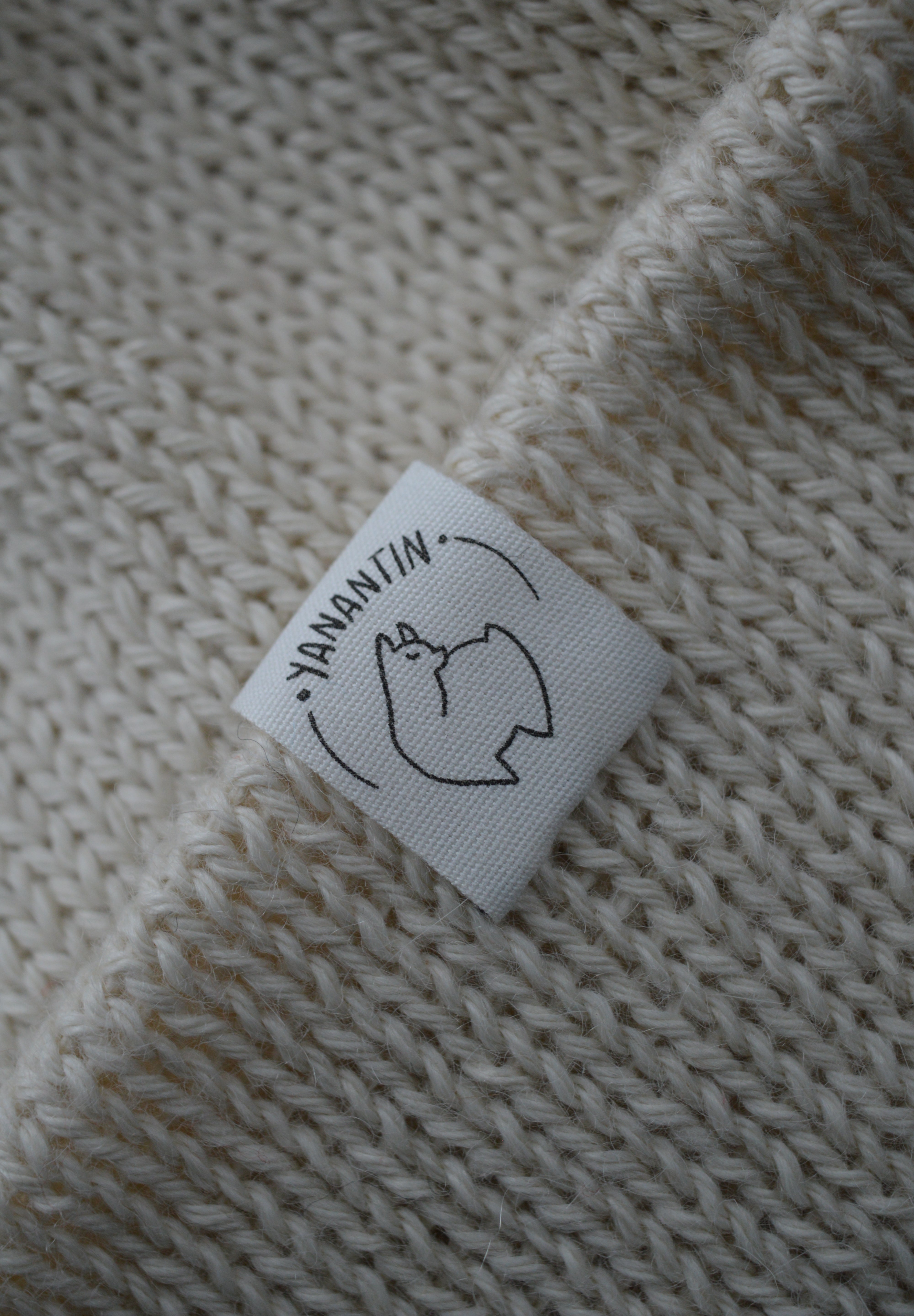 White organic cotton logo of a cute alpaca featuring the brand 'YANANTIN' on a white woolen hat