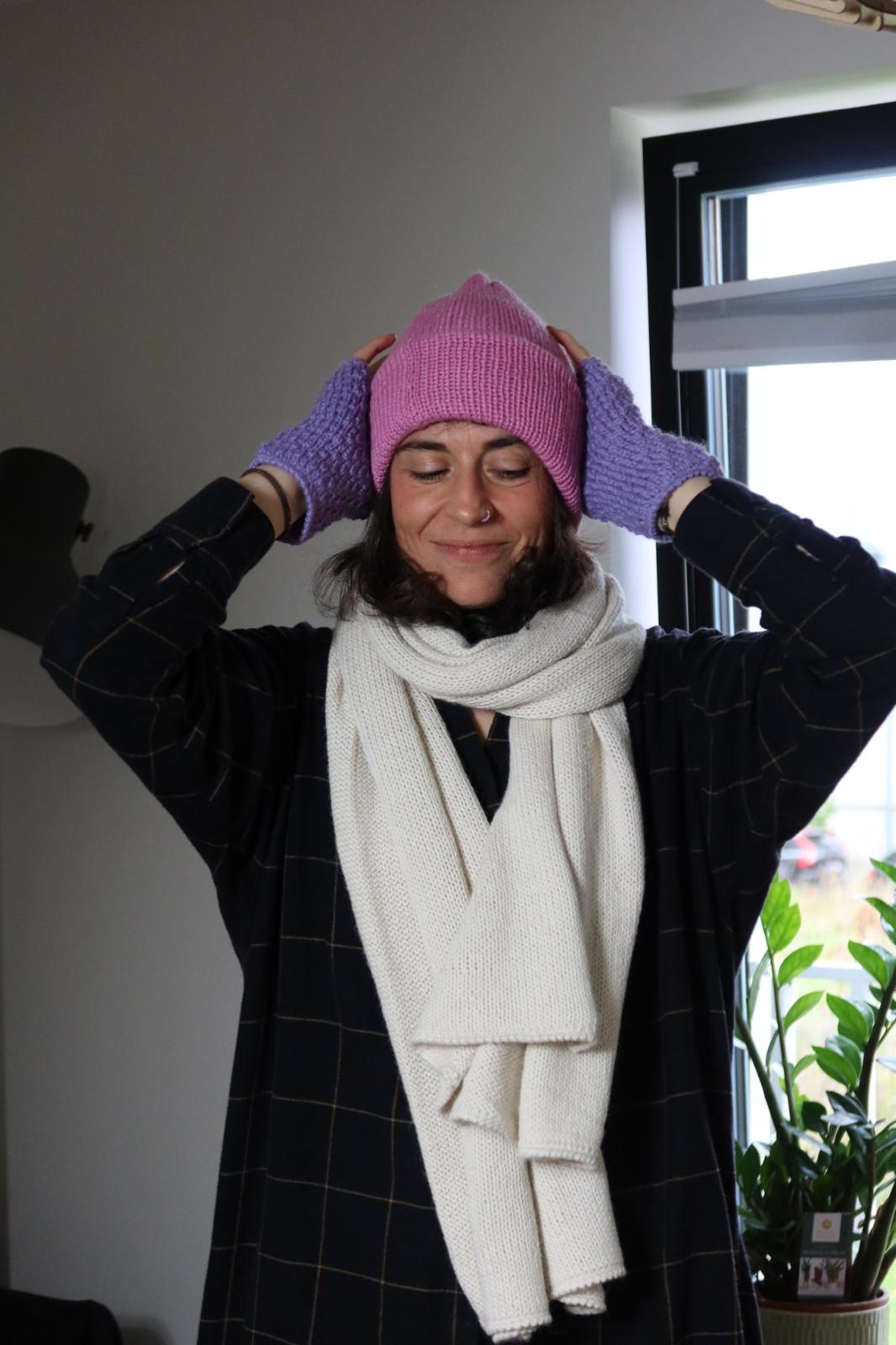 Person wearing a pink knitted beanie and white scarf indoors.