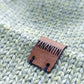 Close-up of the brown vegan leather label on the handmade light green baby hat, highlighting its quality and style.