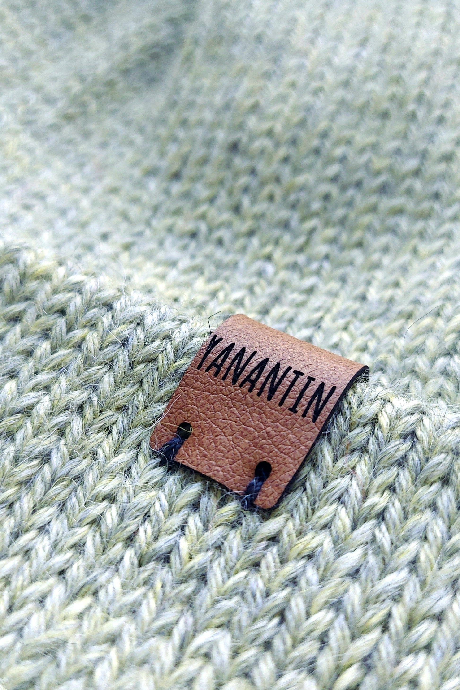 Close-up of the brown vegan leather label on the handmade light green baby hat, highlighting its quality and style.