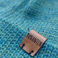 Close-up of the brown vegan leather label on the handmade peacock blue baby hat.