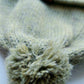 Close-up of the pompom on the handmade light green baby hat, made from soft 100% baby alpaca wool with a foldable edge and brown vegan leather label.
