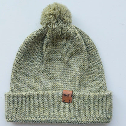 Handmade light green baby hat in soft 100% baby alpaca wool with a pompom, foldable edge, and brown vegan leather label, offering warmth and style.