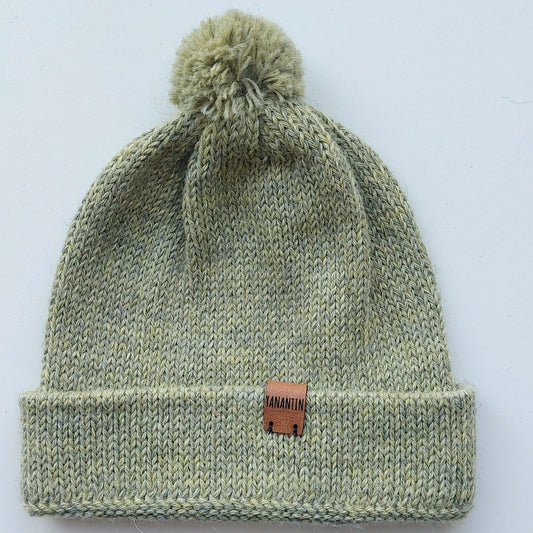 Handmade light green baby hat in soft 100% baby alpaca wool with a pompom, foldable edge, and brown vegan leather label, offering warmth and style.