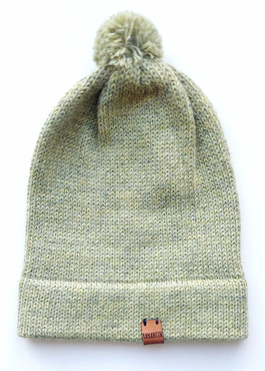 Handmade light green baby hat in soft 100% baby alpaca wool with a pompom, foldable edge, and brown vegan leather label, offering warmth and style.
