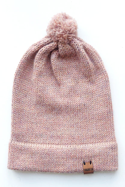 Handmade light pink baby hat in soft 100% baby alpaca wool with a pompom, foldable edge, and brown vegan leather label, offering warmth and comfort.
