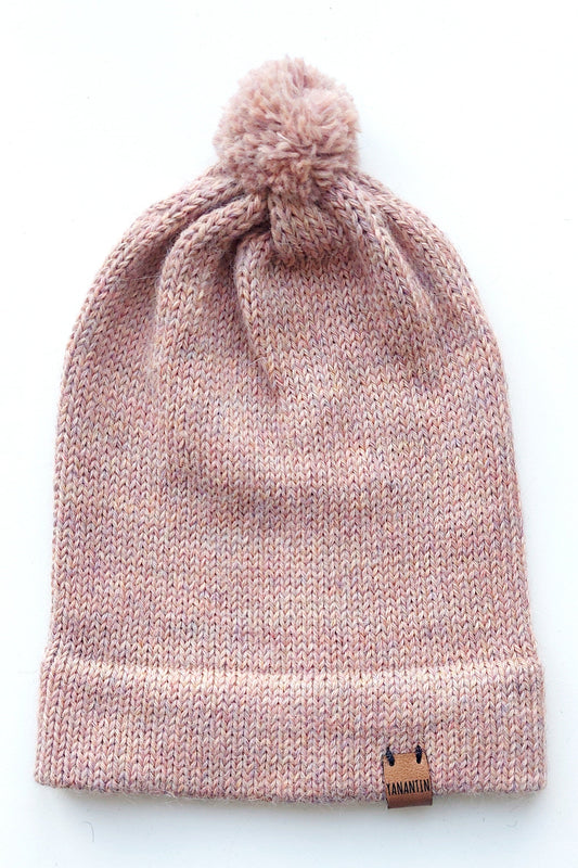 Handmade light pink baby hat in soft 100% baby alpaca wool with a pompom, foldable edge, and brown vegan leather label, offering warmth and comfort.