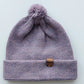 Handmade lila baby hat in soft 100% baby alpaca wool with a pompom, foldable edge, and brown vegan leather label, offering warmth and comfort.