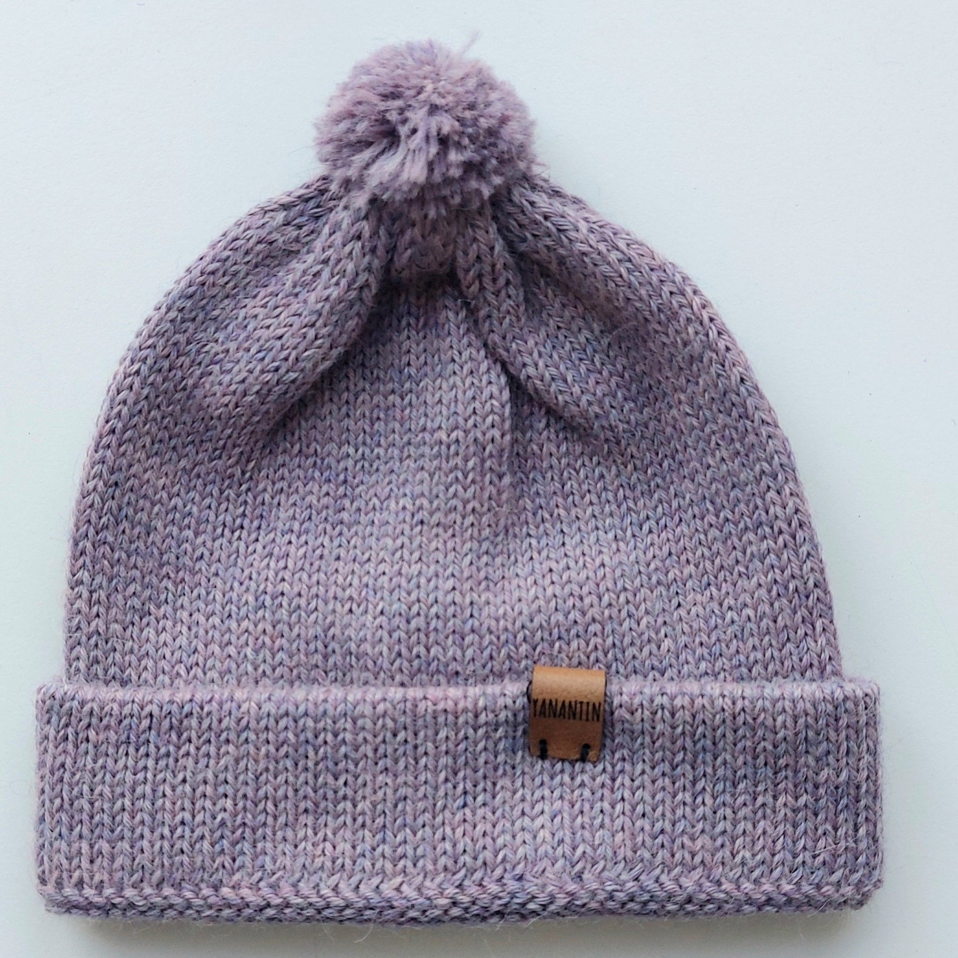 Handmade lila baby hat in soft 100% baby alpaca wool with a pompom, foldable edge, and brown vegan leather label, offering warmth and comfort.