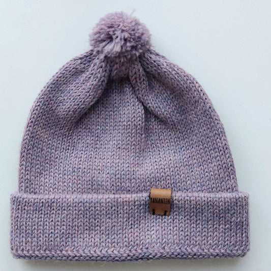 Handmade lila baby hat in soft 100% baby alpaca wool with a pompom, foldable edge, and brown vegan leather label, offering warmth and comfort.