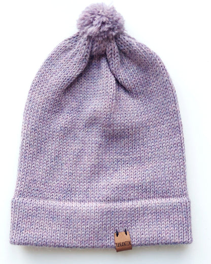 Handmade lila baby hat in soft 100% baby alpaca wool with a pompom, foldable edge, and brown vegan leather label, offering warmth and comfort.
