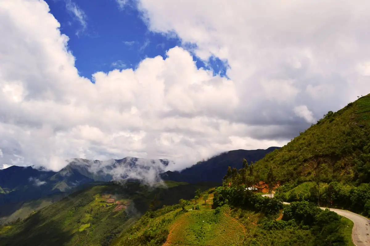 Andean landscape showing mountain road at high altitude. Weather is half cloudy with some bits of blue sky. Beautiful green mountains