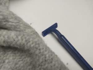 The simplest way to remove a fuzz ball from a woolen garment is by using a razor.